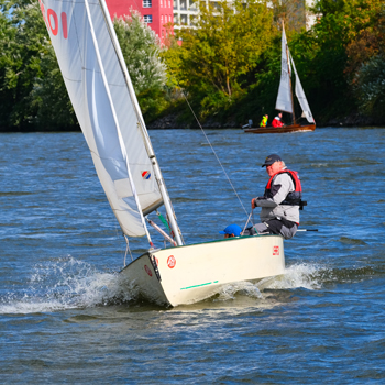 Ein Segler in einem kleinen Boot auf einem Gewässer, im Hintergrund weitere Segelboote. Ein Segler in einem kleinen Boot auf einem Gewässer, im Hintergrund weitere Segelboote.