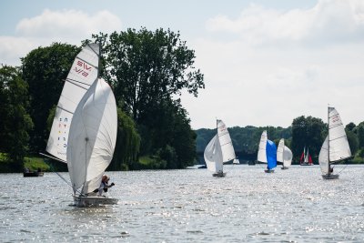 Segelboote auf einem Gewässer, unter blauem Himmel, umgeben von Bäumen und Wiese. Segelboote auf einem Gewässer, unter blauem Himmel, umgeben von Bäumen und Wiese.