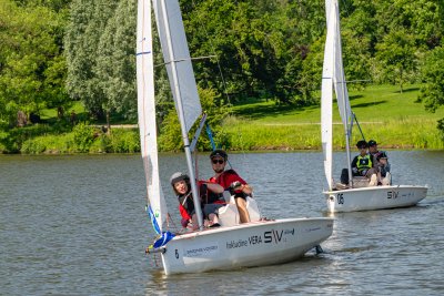 Zwei Segelboote auf einem See. Auf einem Boot sitzen zwei Personen, im Hintergrund ein Park. Zwei Segelboote auf einem See. Auf einem Boot sitzen zwei Personen, im Hintergrund ein Park.