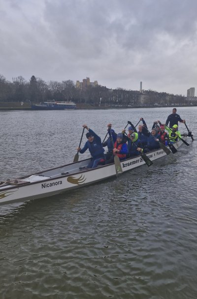 Zehn Personen rudern im Drachenboot auf einem Gewässer an einem bewölkten Tag.