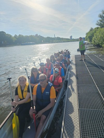 Gruppe von 15 Personen im Drachenboot auf einem Gewässer, sonnige Umgebung, einige tragen Schwimmwesten. Gruppe von 15 Personen im Drachenboot auf einem Gewässer, sonnige Umgebung, einige tragen Schwimmwesten.