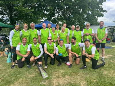 Gruppe von etwa 20 Menschen in grünen Shirts, die im Freien für einen Drachenboot-Wettbewerb posieren.