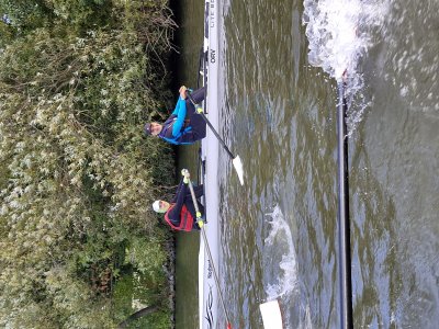 Zwei Personen rudern in einem Boot auf einem ruhigen Gewässer, umgeben von Bäumen.